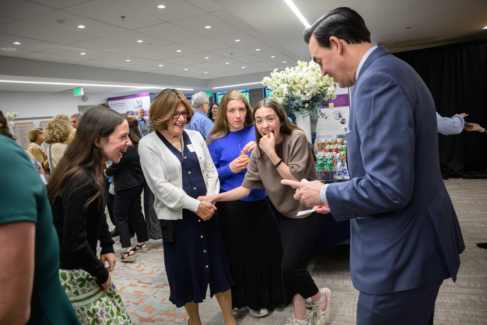 "Mentalist Adam Stone performing strolling close-up magic for a laughing group of guests at a cocktail party"