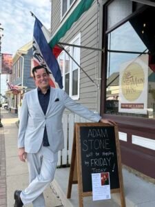 Adam Stone Live Show Promotion Rock Hall Maryland Adam Stone Magic Mentalist Adam Stone Standing in Front of a Chalkboard Sign Announcing His Visit and a Poster Promoting His Upcoming Live Mentalism Show in Rock Hall Maryland