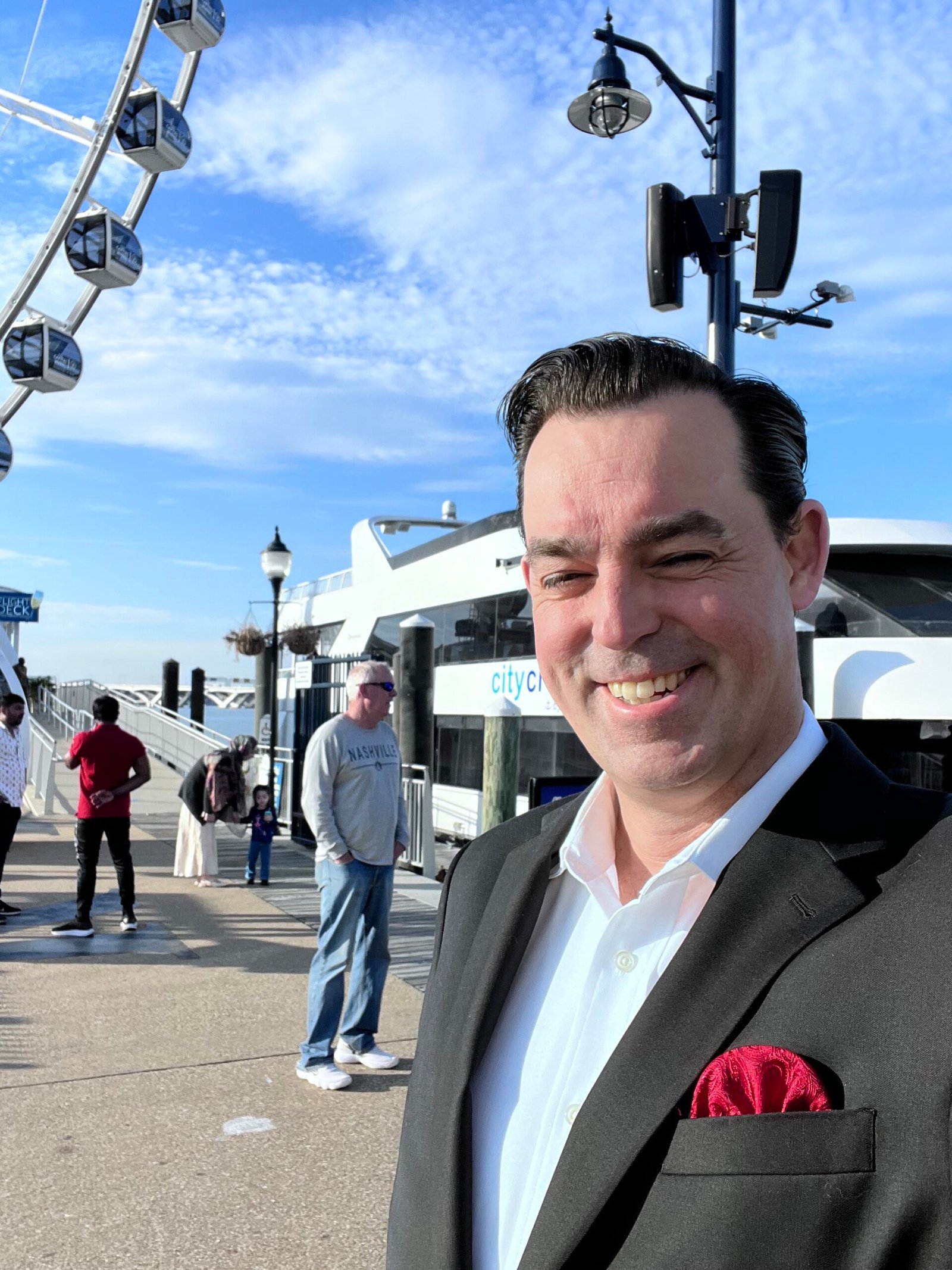 Corporate Mentalist Adam Stone Standing in Front of a Boat at National Harbor with the Capital Wheel Visible in the Background Before Performing Strolling Mentalism and a Stage Show on a Dc Cruise Event